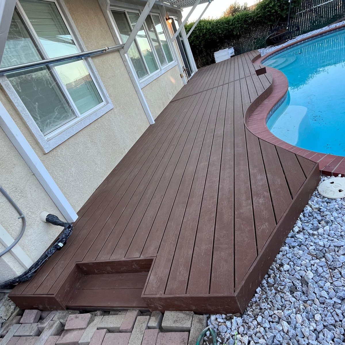 Dark brown composite deck following the curve of a backyard pool
