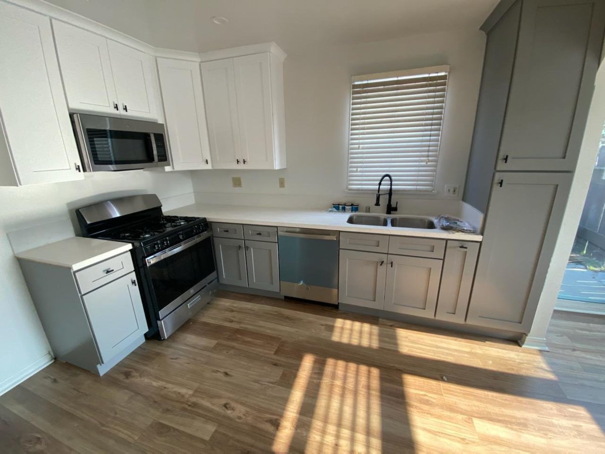 Sunlit white kitchen with gray lower cabinets, stainless range and wood-look flooring