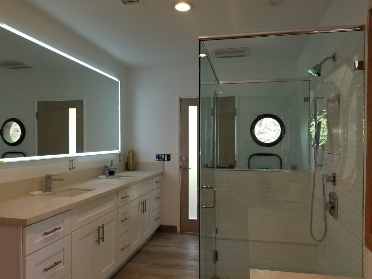 Bathroom with a long white vanity, backlit mirror and frameless glass shower