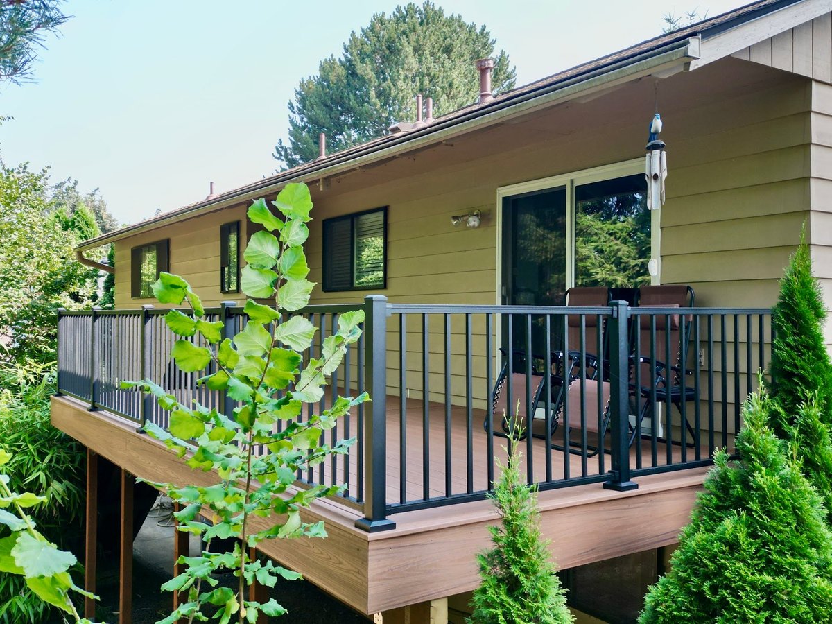 Elevated composite deck with black metal railings on a sloped lot behind a two-story home