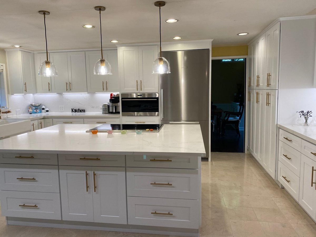 White kitchen with a large quartz island, gold hardware, glass pendant lights and floor-to-ceiling pantry cabinets