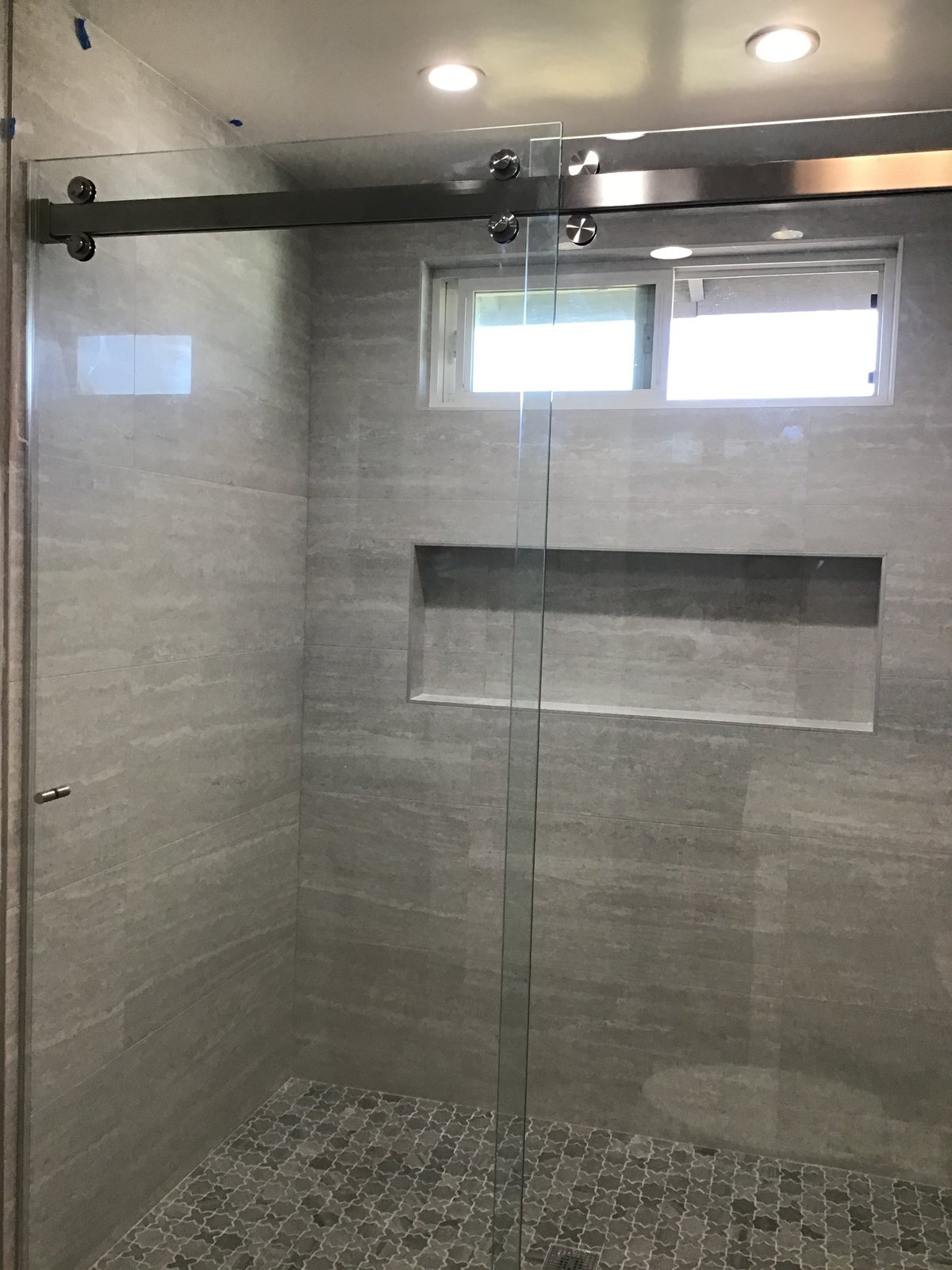 Walk-in shower with gray porcelain wall tile, a long recessed niche and a sliding glass door