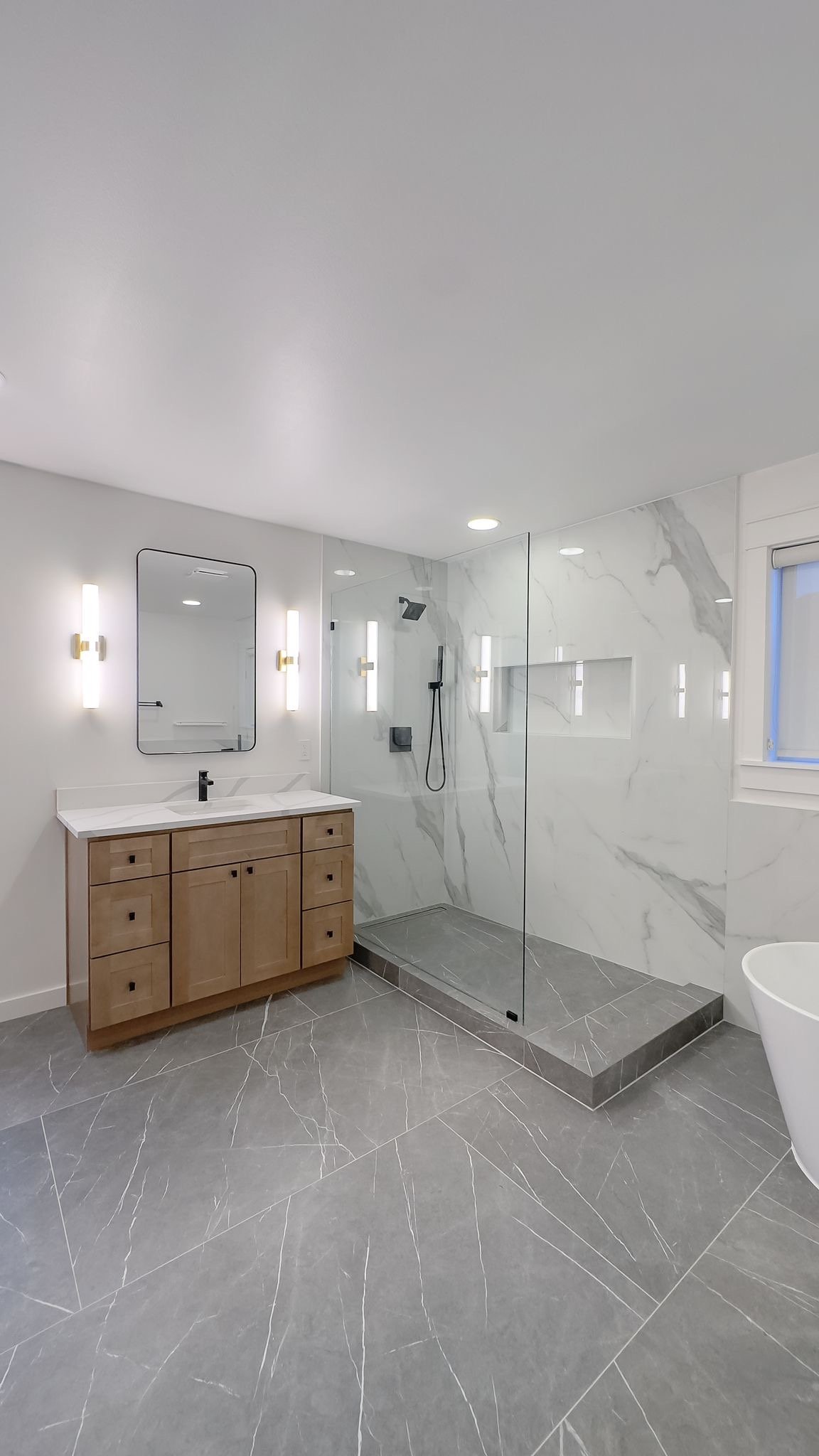 Compact remodeled bathroom with a wood vanity, frameless glass shower and freestanding tub
