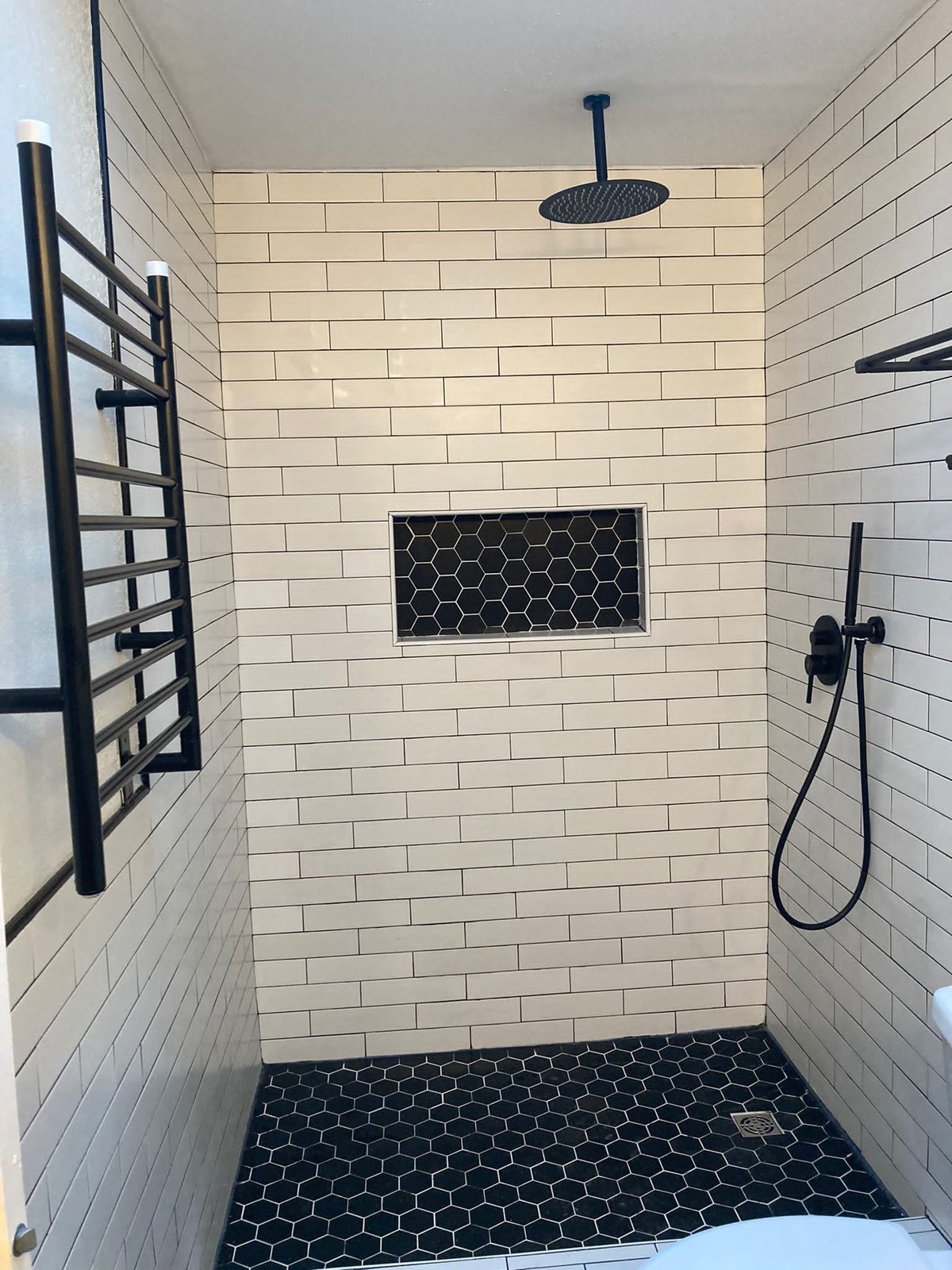 Subway-tile shower with a black hexagon tile floor, recessed niche and matte black fixtures