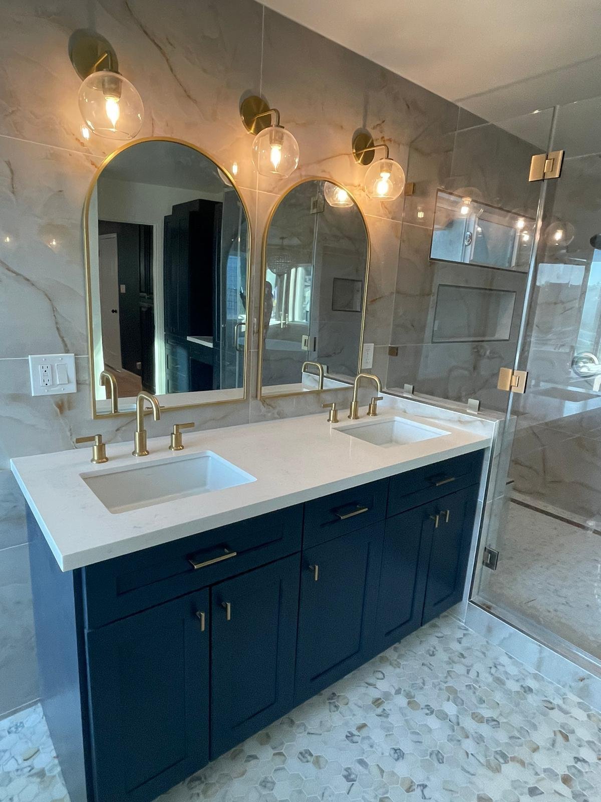 Navy double vanity with quartz top, brass faucets, arched mirrors and globe sconces