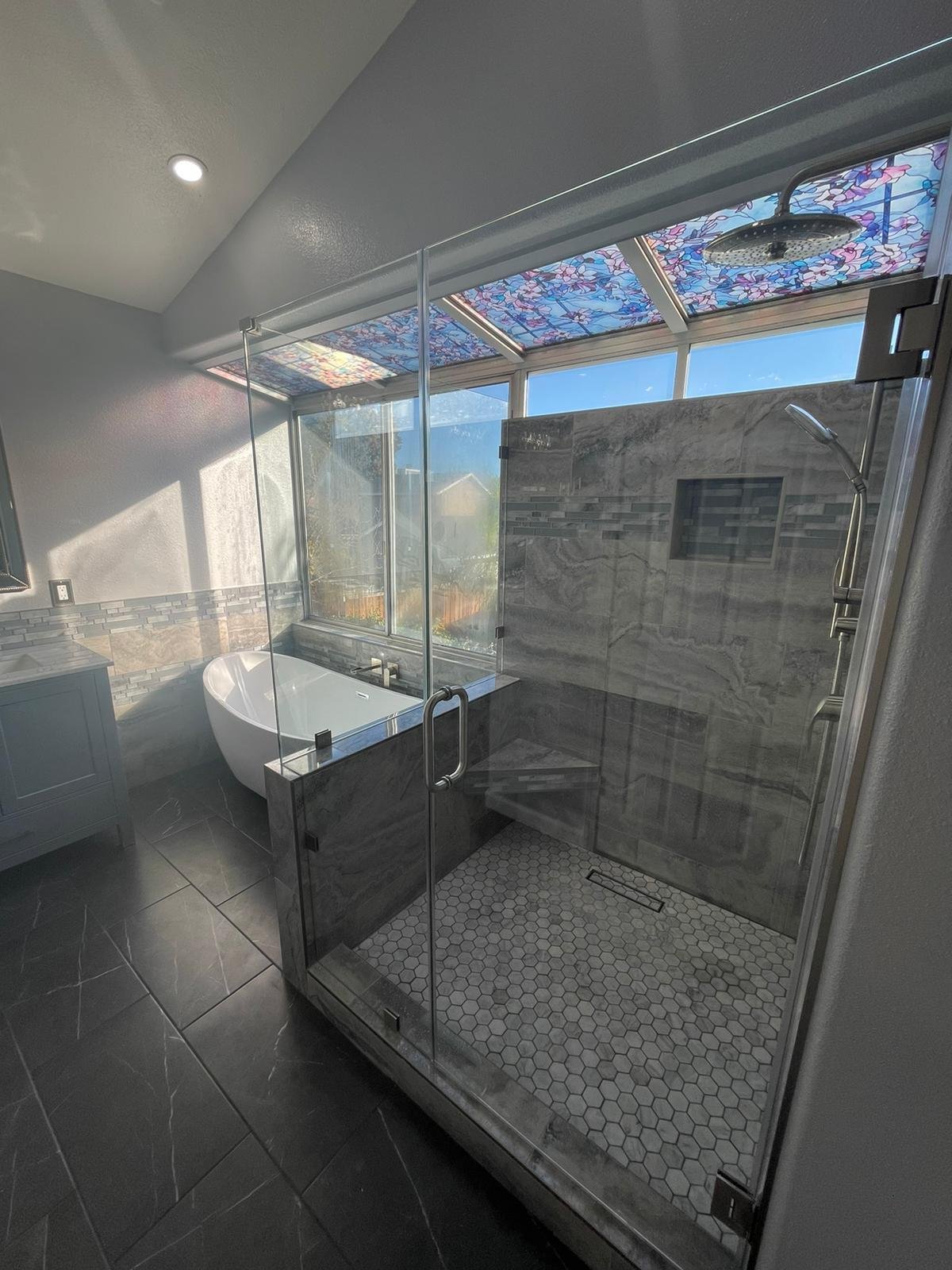 Glass-enclosed walk-in shower with a hexagon tile floor beside a freestanding tub under decorative glass ceiling panels