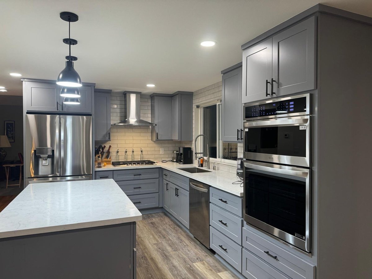 Gray shaker kitchen with a quartz island, black pendant lights and stainless wall ovens