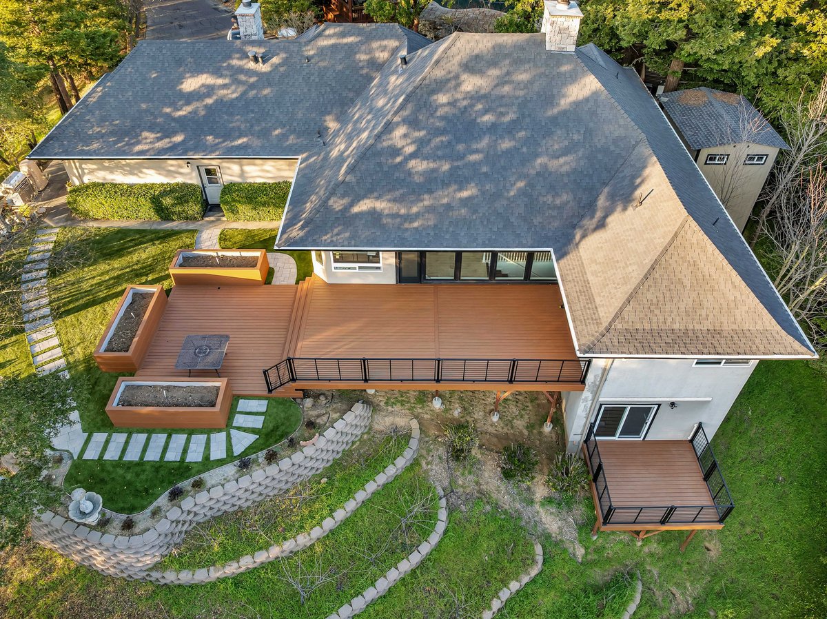 Aerial view of a hillside home with a new composite deck, planters, stone paths and retaining walls