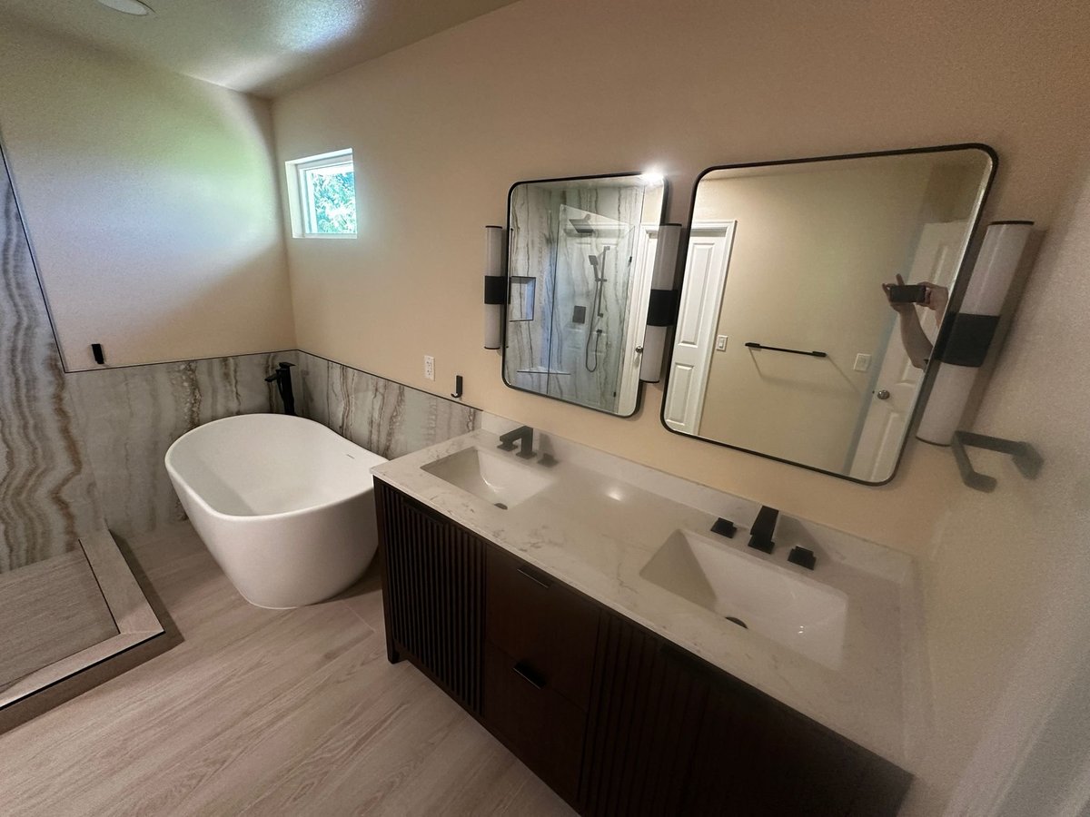 Remodeled bathroom with a freestanding tub, dark double vanity and two framed mirrors