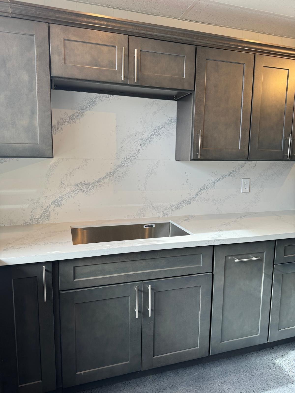 Full-height veined quartz backsplash above an undermount sink and charcoal shaker cabinets