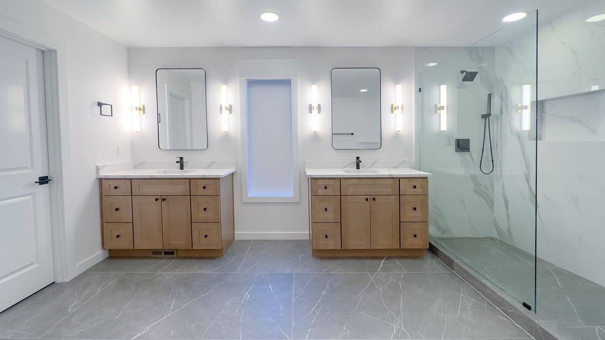 Bathroom with two wood vanities, rectangular mirrors, sconces, large-format tile and a frameless glass shower