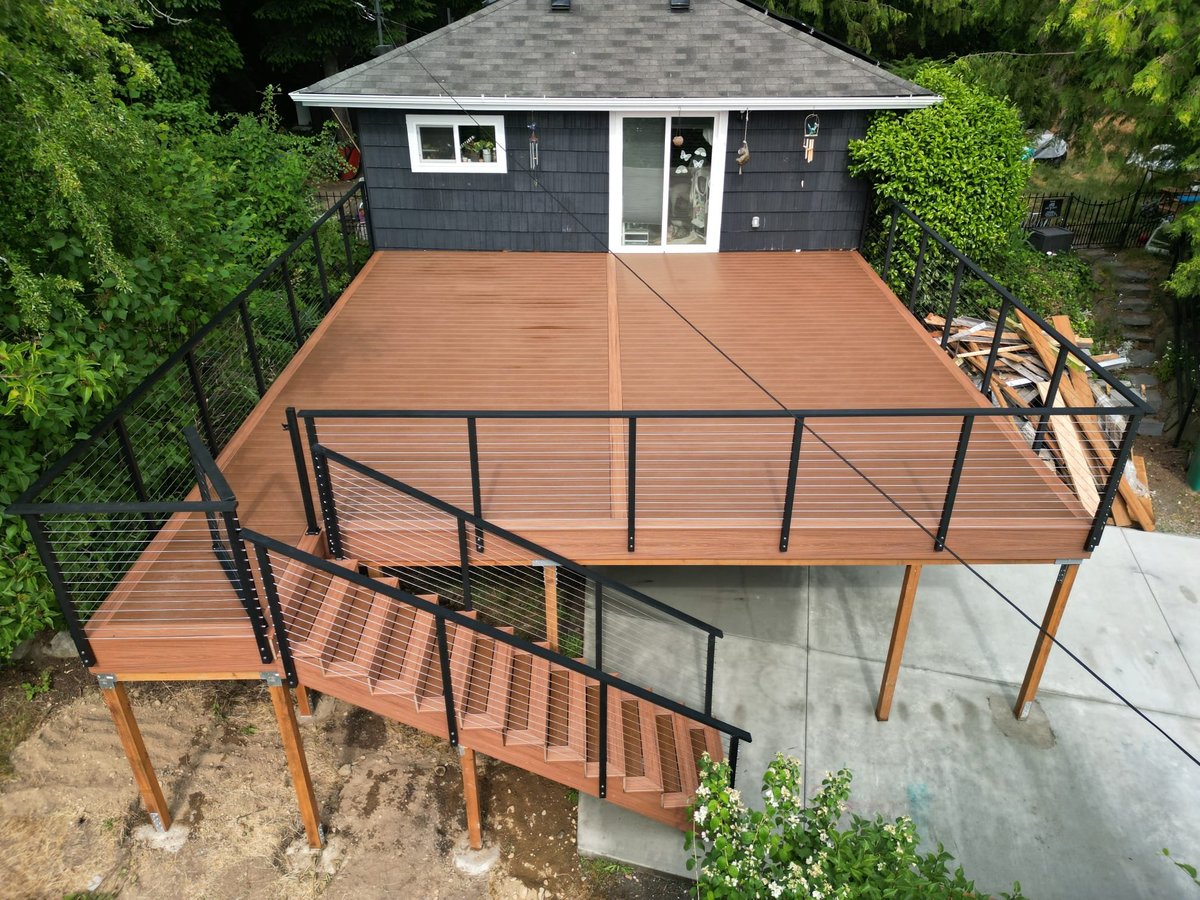 Newly framed elevated deck on posts with stairs and cable railing behind a home