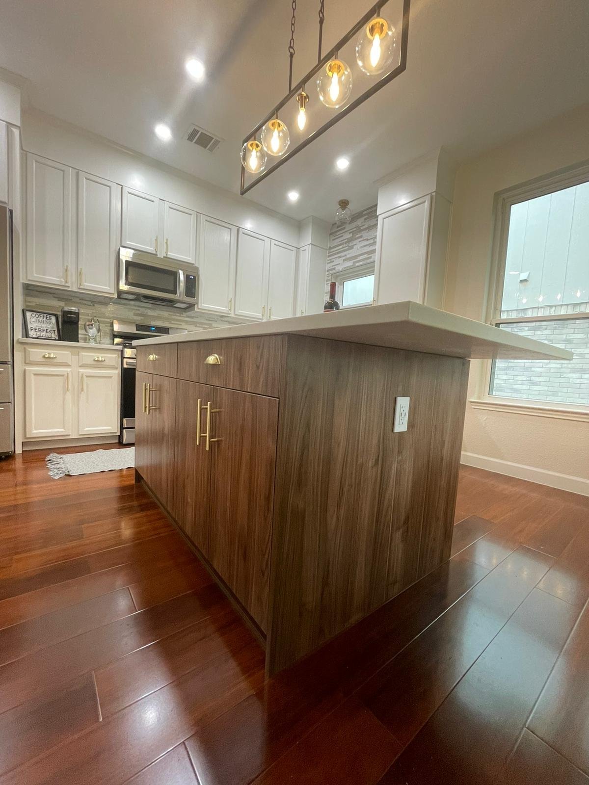 Kitchen with a large walnut-finish island, quartz top, linear pendant light and hardwood floors