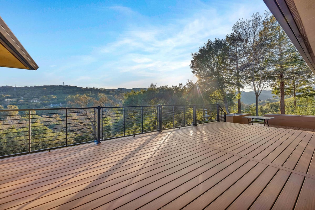 Composite deck with black cable railing overlooking wooded hills at sunset
