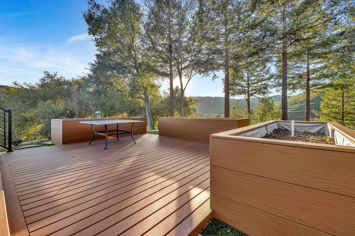 Composite deck with built-in planters and an outdoor dining table among tall trees on a hillside