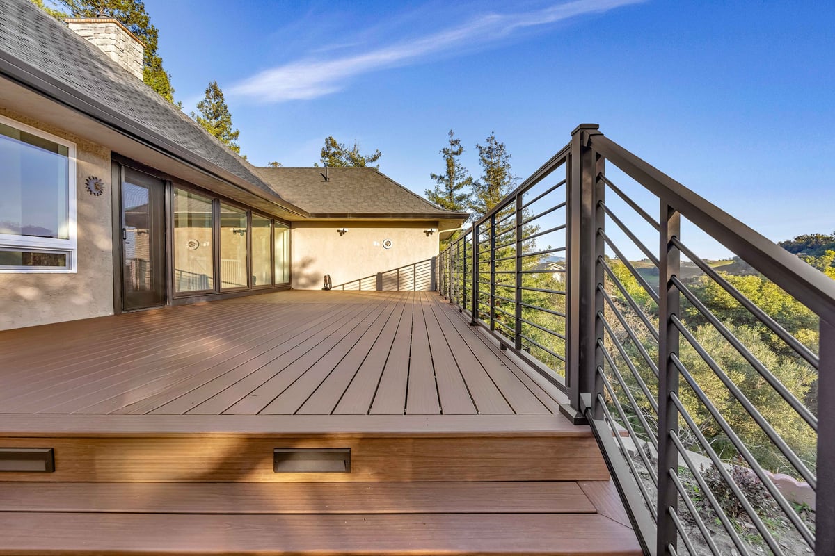 Hillside composite deck with horizontal metal railing along a home with a view of wooded hills