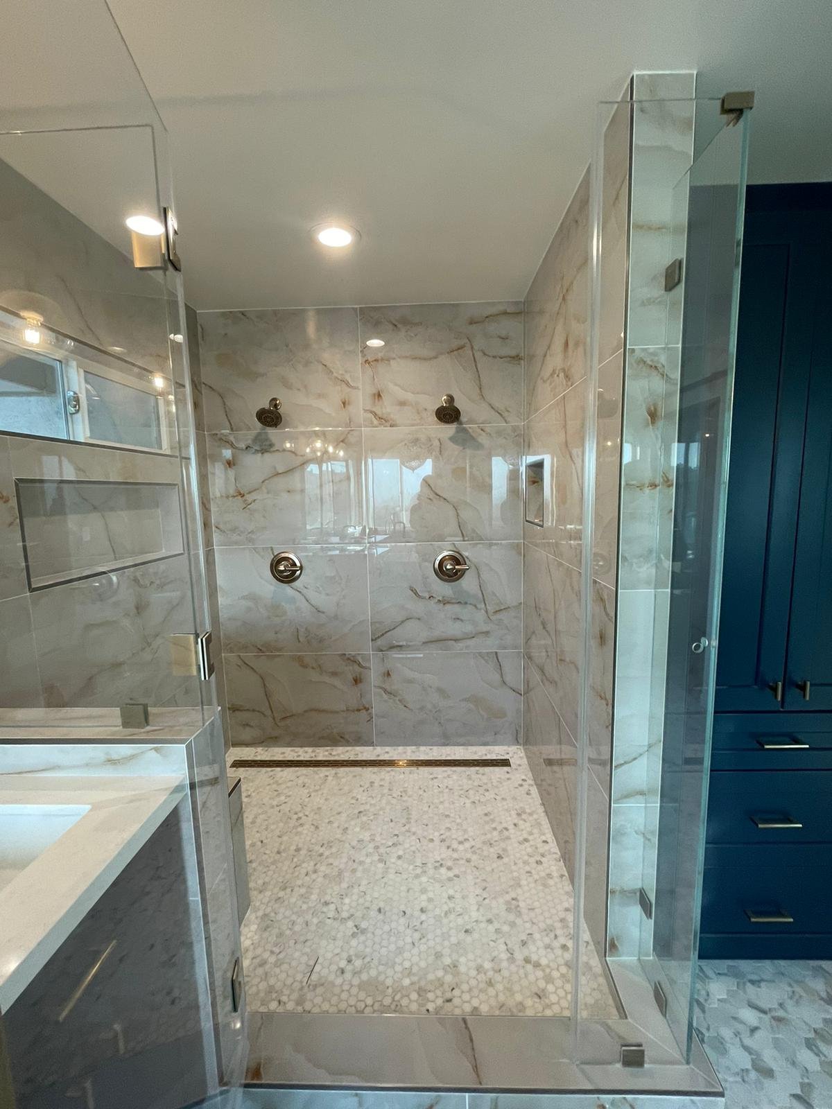 Walk-in shower with marble-look tile, a pebble floor, glass enclosure and navy cabinetry