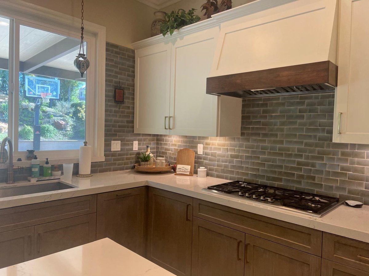 Kitchen with white upper cabinets, a wood range hood, gray subway tile and wood lower cabinets