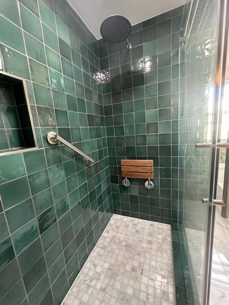 Green-tile walk-in shower with a grab bar and a fold-down teak shower seat