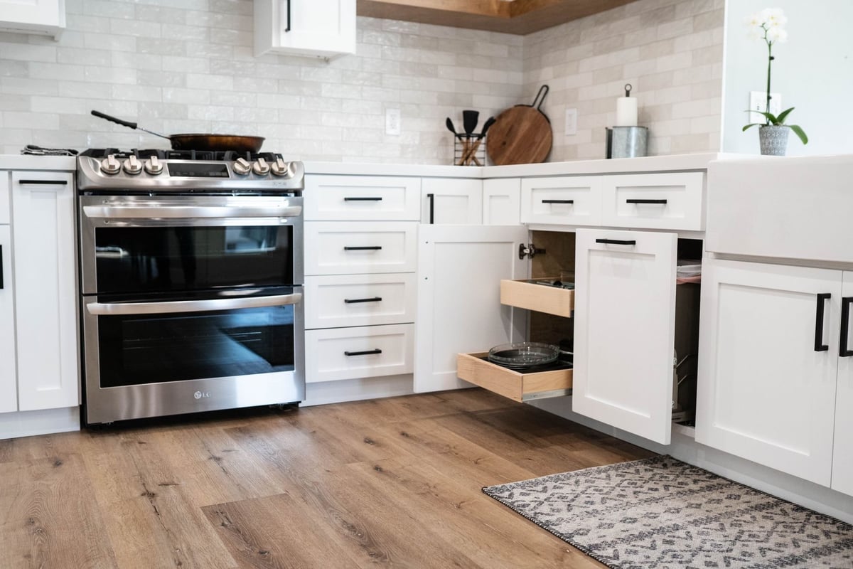 White shaker cabinets with pull-out drawers open beside a stainless double-oven range