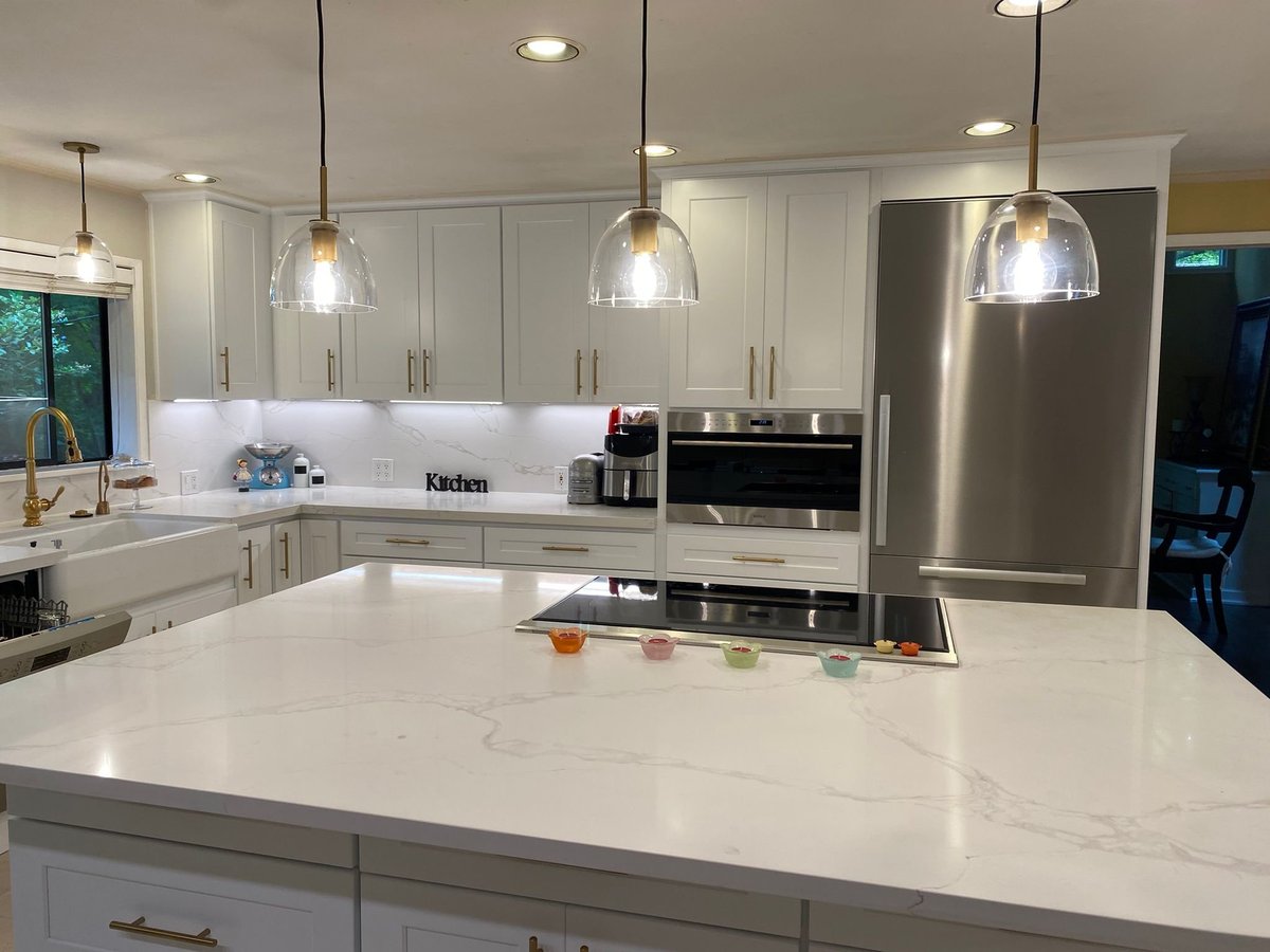 White shaker kitchen with a large quartz island, glass pendant lights and stainless appliances