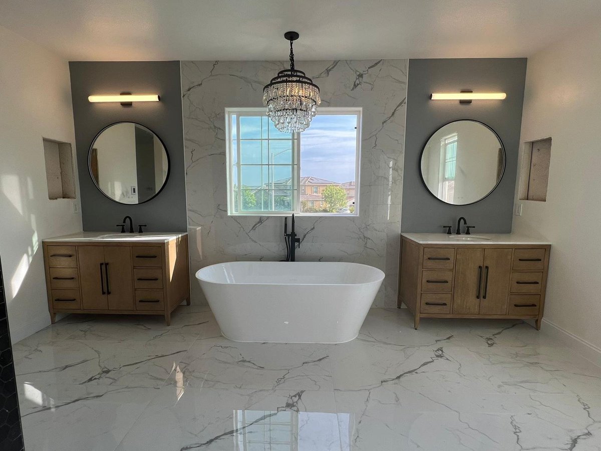 Remodeled primary bathroom with two wood vanities, round mirrors, a freestanding tub and a crystal chandelier
