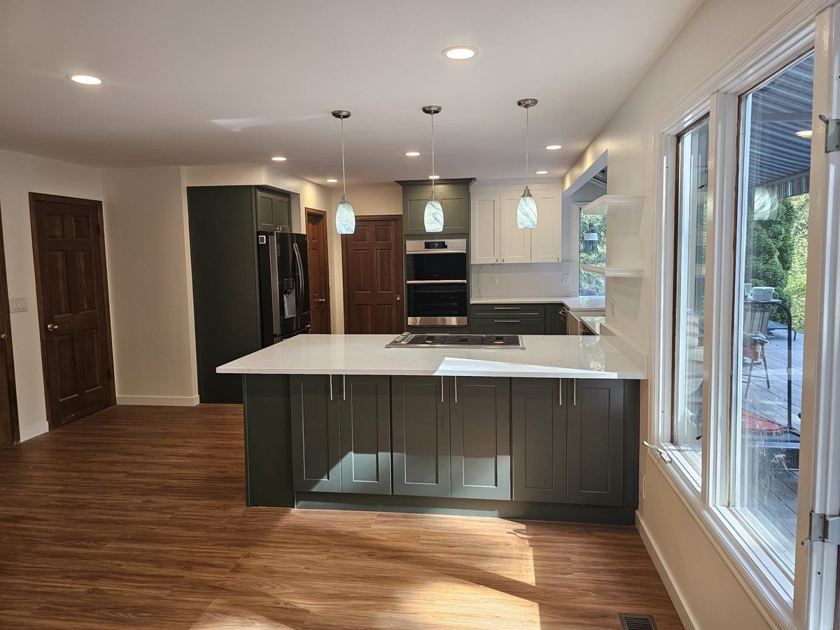 Kitchen with a large quartz island and green shaker cabinets, pendant lights and windows to the yard